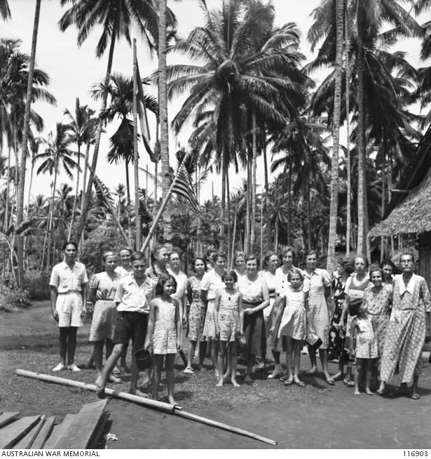 September 1945 — Para interniran perempuan di Kamp Interniran Perempuan Airmadidi berkumpul di bawah bendera Belanda, Britania Raya, dan Amerika Serikat sesaat setelah dibebaskan dari tahanan Jepang oleh pasukan Manado Force. Momen ini menandai berakhirnya penderitaan mereka setelah Perang Dunia II. Sumber foto: Australian War Memorial (AWM - Engel Yong)